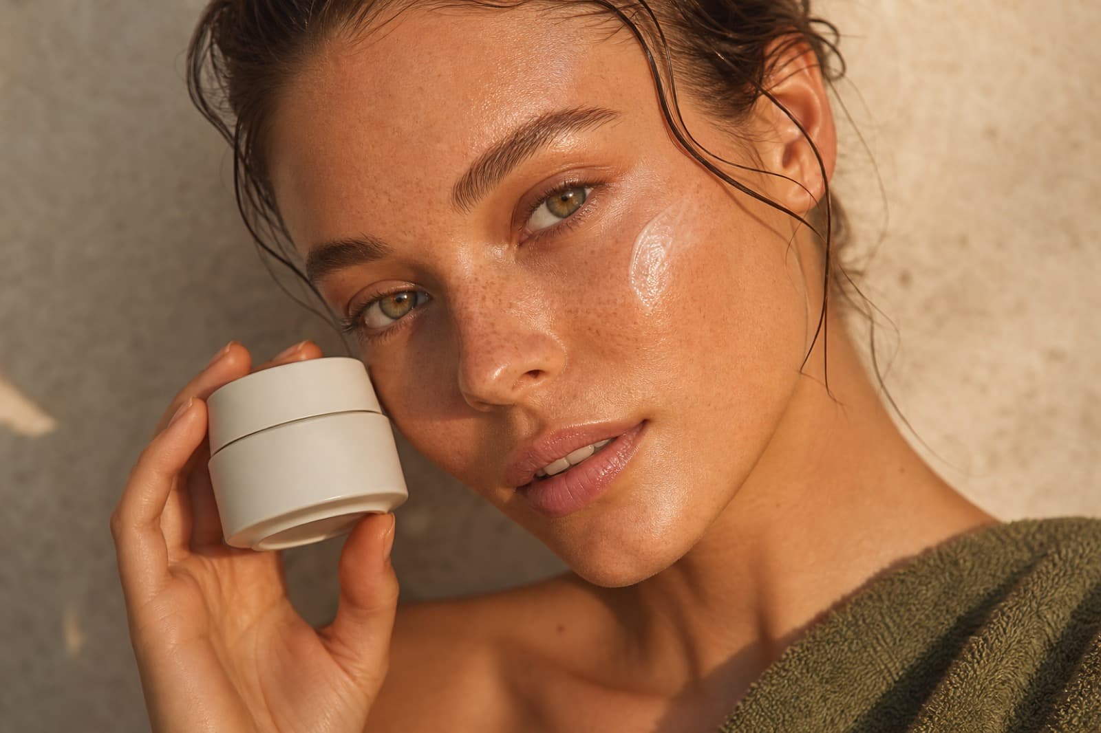 Model applying Lumière moisturizer in editorial beauty lighting